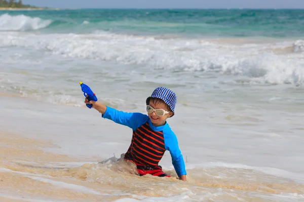 Mały chłopiec bawi się pistoletem na wodę na plaży — Zdjęcie stockowe
