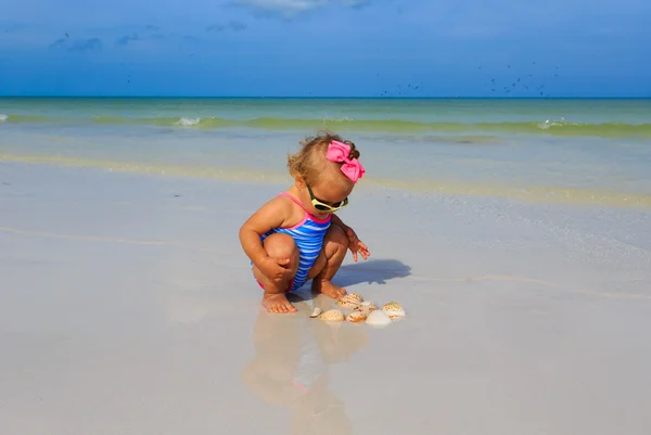 Schattig klein meisje spelen met schelpen op het strand — Stockfoto