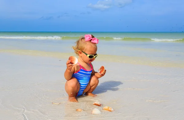 Mignonne petite fille jouer avec des coquillages sur la plage — Photo