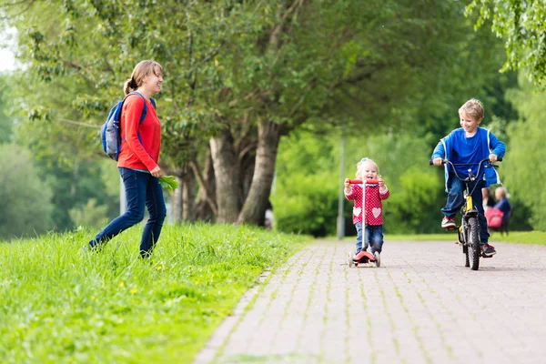 Счастливая мать с двумя детьми на скутере и велосипеде в парке — стоковое фото