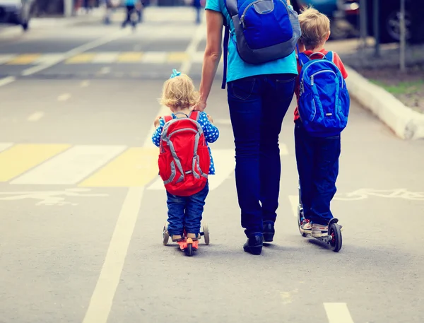 Mother with kids on scooters riding along the road — Stock Photo, Image