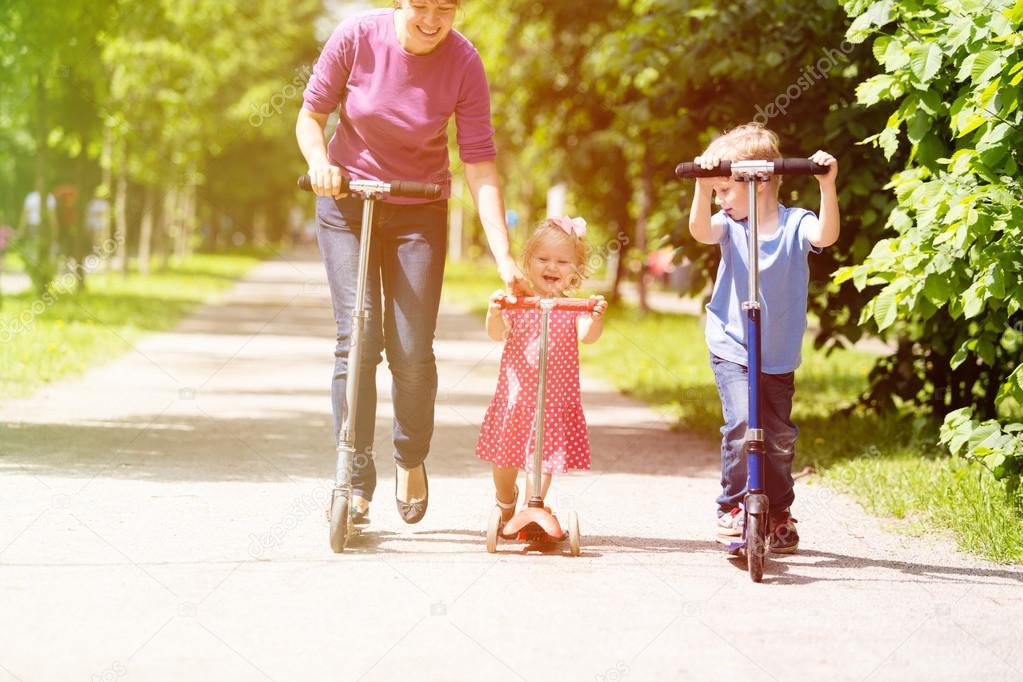 mother with kids riding scooter in summer