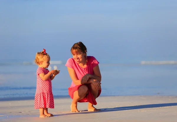 Moeder en kleine dochter verzamelen van schelpen op het strand — Stockfoto