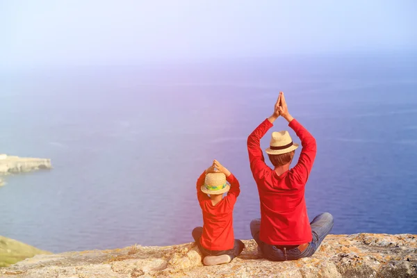 Father and son doing yoga in mountains at the sea — Stock Photo, Image