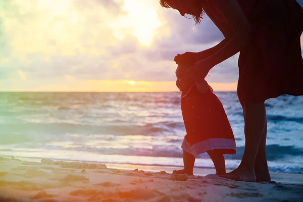 Mãe e filhinha andando na praia ao pôr do sol — Fotografia de Stock