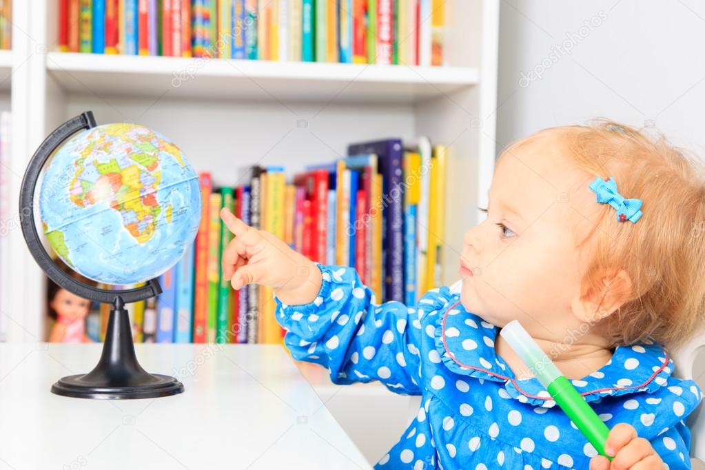 little girl pointing to world globe in classroom