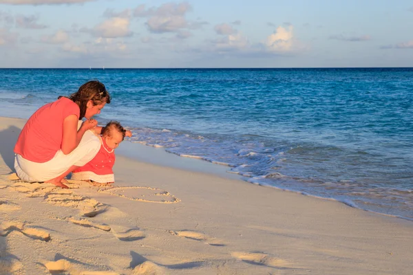 Madre e hija pequeña dibujando corazón en la playa — Foto de Stock