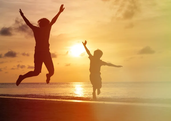 Pai e filho pulando na praia do pôr do sol — Fotografia de Stock