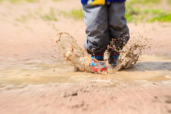 Child wearing red rain boots jumping into a puddle — Stock Photo, Image