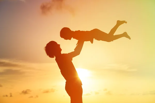 Vader en kleine zoon silhouetten spelen bij zonsondergang — Stockfoto