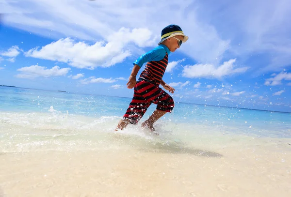 Piccolo ragazzo spruzzi d'acqua sulla spiaggia tropicale — Foto Stock