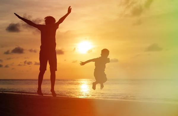 Pai e filho pulando na praia do pôr do sol — Fotografia de Stock