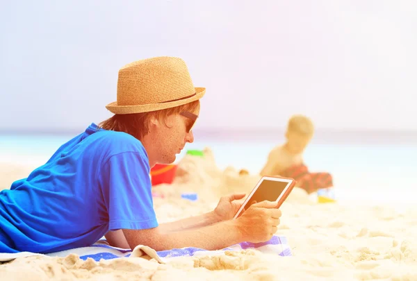 Father looking at touch pad while son play on beach — Stock Photo, Image