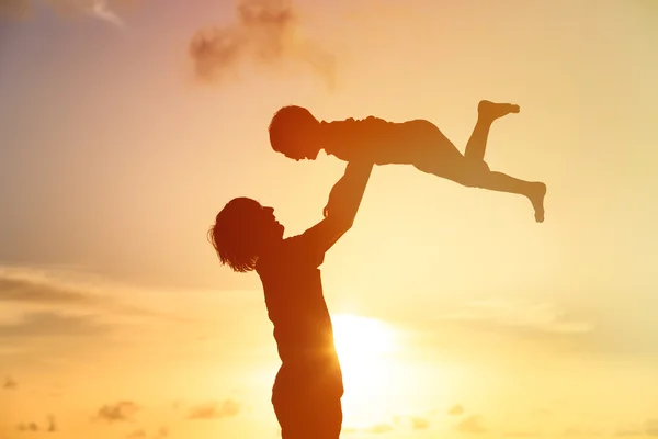 Vader en kleine zoon silhouetten spelen bij zonsondergang — Stockfoto