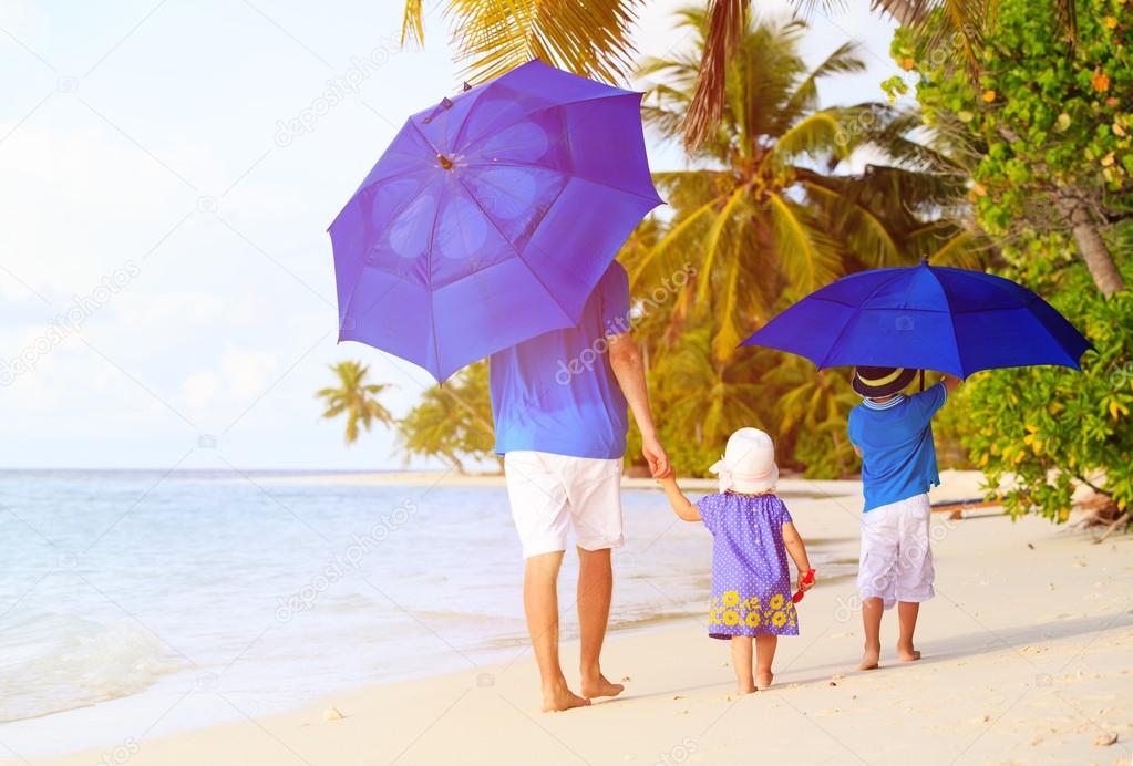 Father and kids at beach with umbrellas to hide from sun