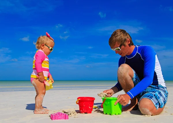 Отец и маленькая дочь играют с песком на пляже — стоковое фото