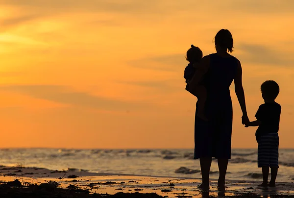 Mãe e dois filhos andando na praia ao pôr do sol — Fotografia de Stock