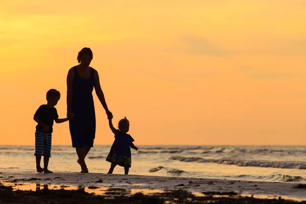 Mãe e dois filhos andando na praia ao pôr do sol — Fotografia de Stock