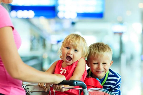 Feliz linda niña y niño en el aeropuerto en el carrito de equipaje — Foto de Stock