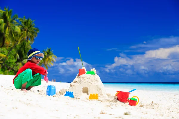 Mały chłopiec budujący zamek z piasku na tropikalnej plaży piasek — Zdjęcie stockowe