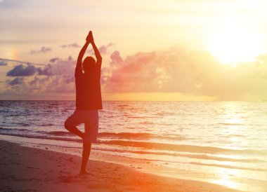 Gün batımında yoga yaparken genç adam silüeti