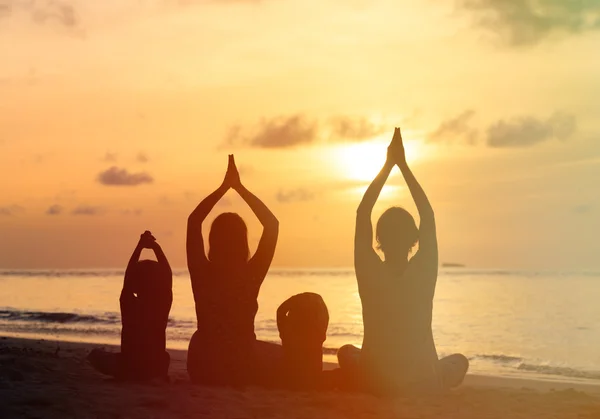 Siluetas familiares haciendo yoga al atardecer — Foto de Stock