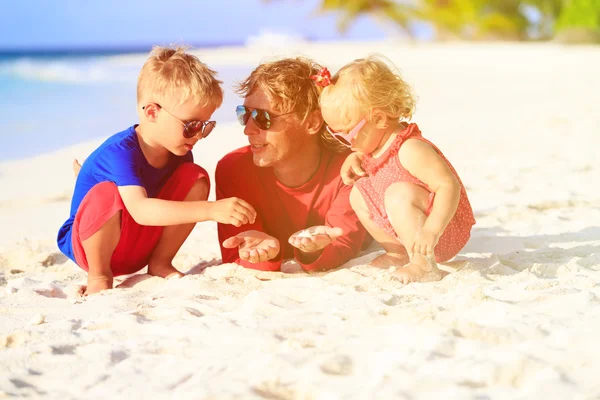 Vader en twee kinderen spelen met zand op het strand — Stockfoto