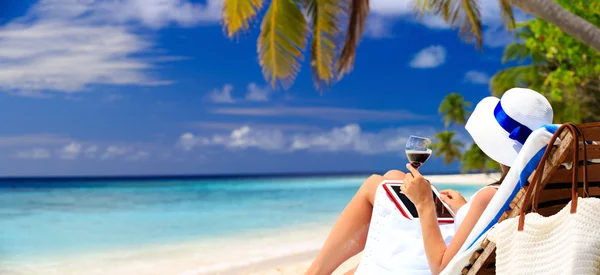 Woman drinking wine and looking at touch pad on beach — Stock Photo, Image