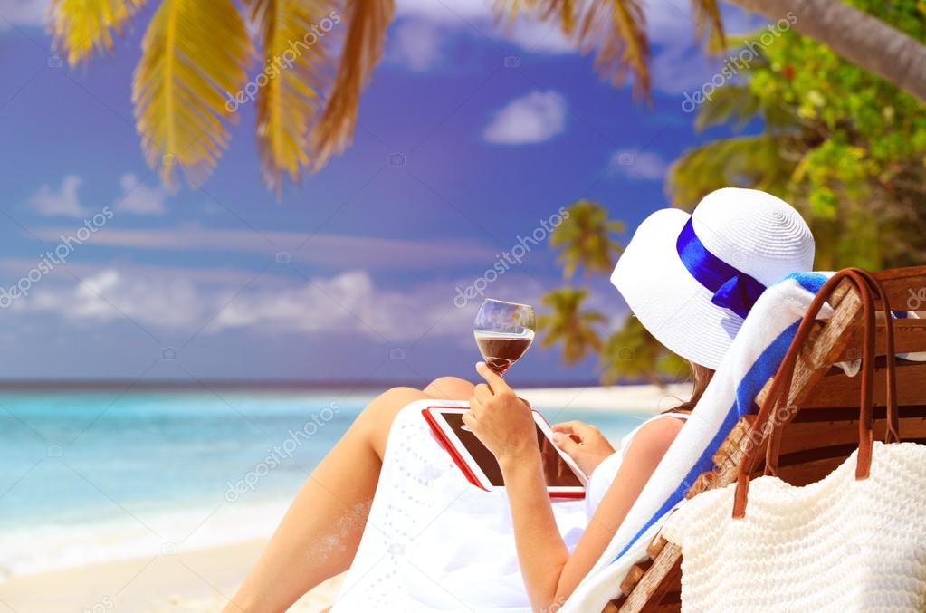 woman drinking wine and looking at touch pad on beach