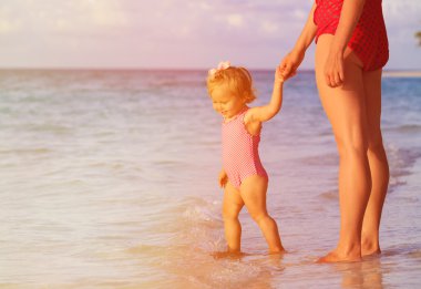 Anne ve küçük kızı günbatımı Sahilde yürüyüş