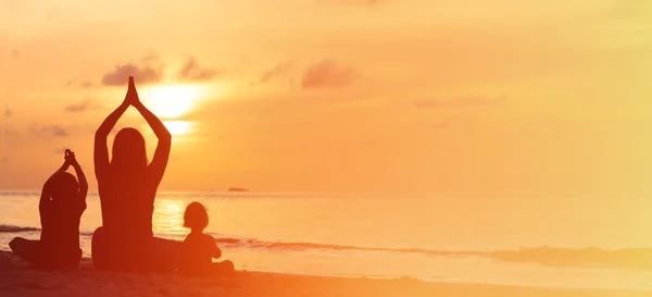 Silhueta de mãe e crianças fazendo ioga no pôr do sol mar — Fotografia de Stock