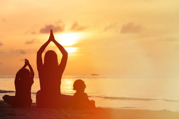 Anne ve çocuklar gün batımında yoga yaparken silüeti