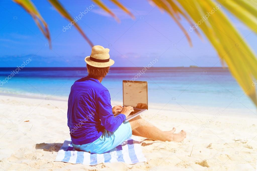 young man with laptop on tropical beach