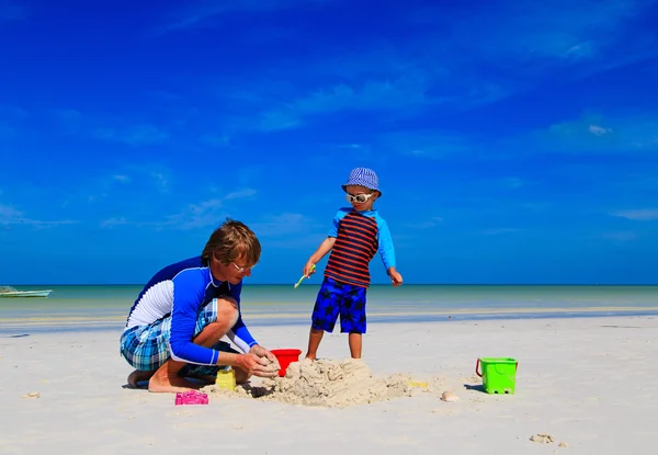 Vader en zoon gebouw zand kasteel op tropisch strand — Stockfoto
