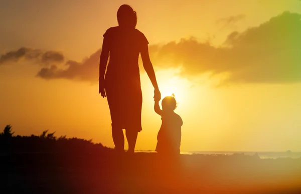 Mor och liten dotter går på stranden vid solnedgången — Stockfoto