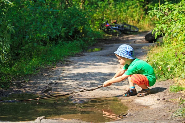 Niño jugando con un palo en el charco de agua al aire libre — Foto de Stock