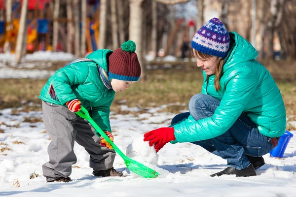 Mother and son building snowman in winter — Stock Photo, Image