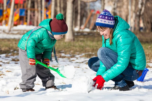 Мать и сын строят снеговика зимой — стоковое фото