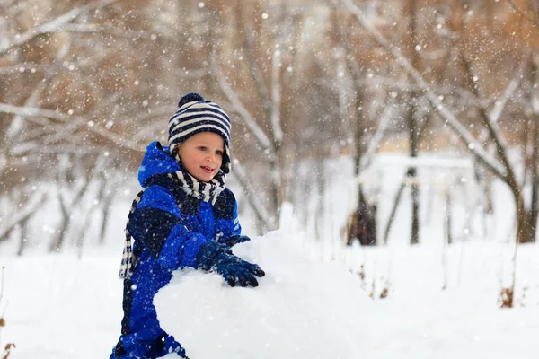 Маленький хлопчик будує сніговика в зимовому парку — стокове фото