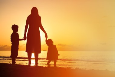 Anne ve iki çocuğu batımında sahilde yürüyüş
