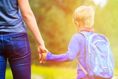 Mother holding hand of little son with backpack outdoors