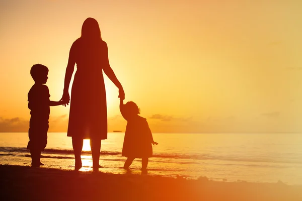 Mère et deux enfants marchant sur la plage au coucher du soleil — Photo