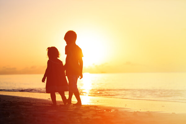 мальчик и девочка прогуливаются по пляжу на закате
