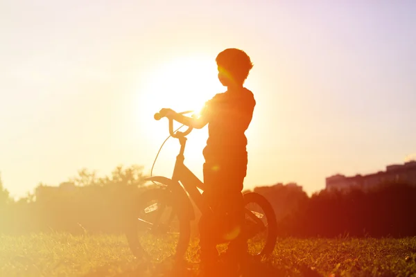 Menino pedalando bicicleta ao pôr do sol — Fotografia de Stock