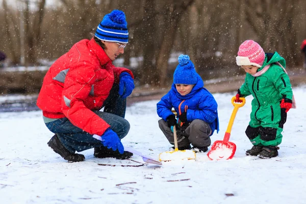 Отец и дети копают снег в зимнем парке — стоковое фото