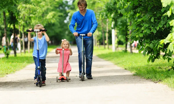 Pai com crianças montando scooters no verão — Fotografia de Stock
