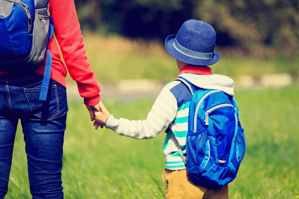 Mãe segurando mão de pequeno filho com mochila ao ar livre — Fotografia de Stock