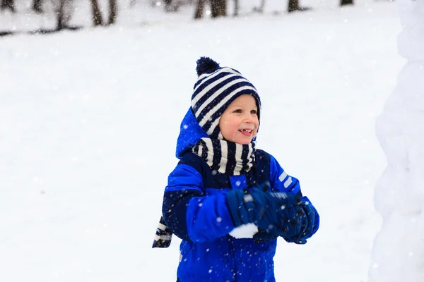 Bonitinho menino edifício boneco de neve no inverno — Fotografia de Stock