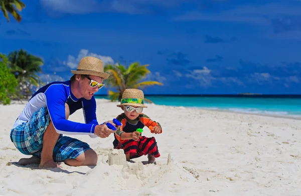 Far och son leker med vattenpistoler på stranden — Stockfoto