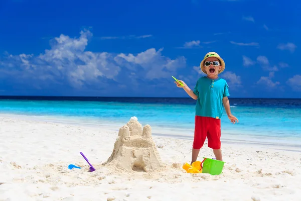 Niño feliz con castillo de arena construido en la playa —  Fotos de Stock